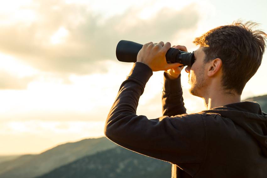 Mann schaut mit Fernglas in die Landschaft