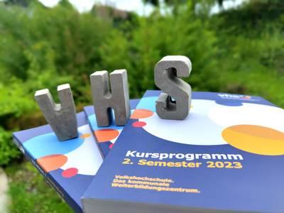 VHS-Prgrammhefte, darauf der Schriftzug VHS aus Beton-Buchstaben