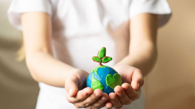 Ein Kind hält eine Weltkugel mit einer Pflanze schützend in seiner Hand