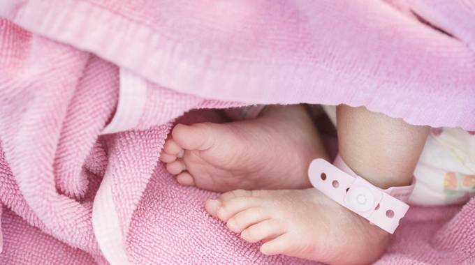 Neugeborenes Mädchen mit rosa Bändchen am Fuß