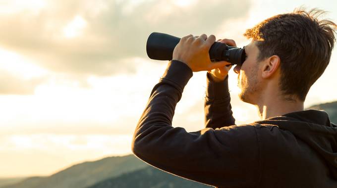 Mann schaut mit Fernglas in die Landschaft