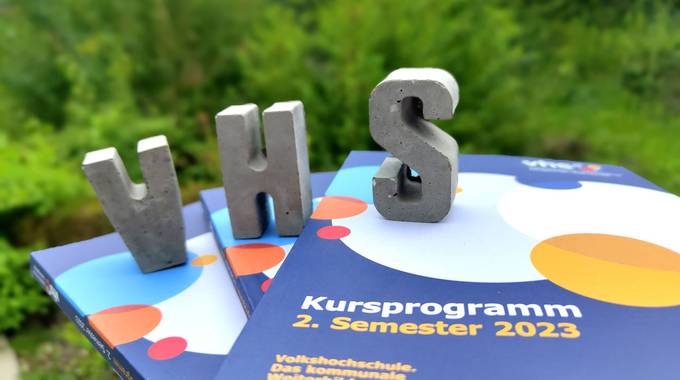 VHS-Prgrammhefte, darauf der Schriftzug VHS aus Beton-Buchstaben