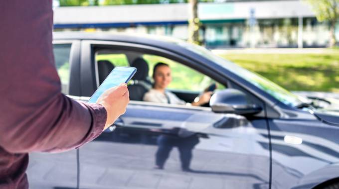 Ein Auto wartet auf einen Mitfahrer, der ein smartphone mit geöffneter App in der Hand hält