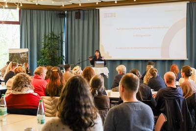 Über 100 Fachkräfte aus Medizin, Bildung, Jugendhilfe, Beratung, Staatsanwaltschaft und Polizei kamen beim Auftakt „Netzwerk Kinderschutz“ zusammen, um die Weichen für eine engere Zusammenarbeit zu stellen. © Stadt Königswinter/Pressestelle In einem Saal referiert eine Frau, vor ihr eine Gruppe von Menschen