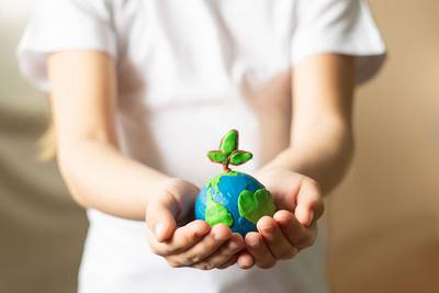 Ein Kind hält eine Weltkugel mit einer Pflanze schützend in seiner Hand