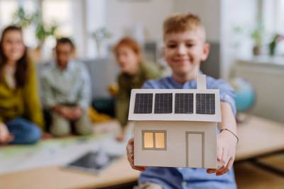 Ein Junge zeigt ein gebasteltes Papierhaus mit PV-Anlage in die Kamera