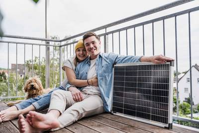 Ein nunges Paar mit Hund sitzt auf dem Boden ihres Balkons, daneben ein Solarmodul
