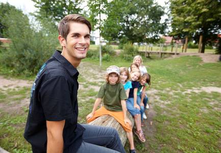 Junger Mann sitzt lachend vor einer Gruppe von Kindern