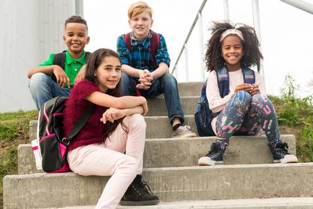 Vier Kinder sitzen auf einer Schultreppe und schauen nach vorne
