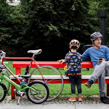 Vater und Kind sitzen auf einer Bank, daneben Fahrräder