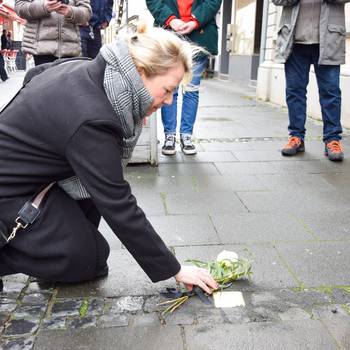 Bürgermeisterin Heike Jüngling kniet vor dem Stolperstein für Irmgard Stefanie Steinhardt in der Hauptstraße 380.