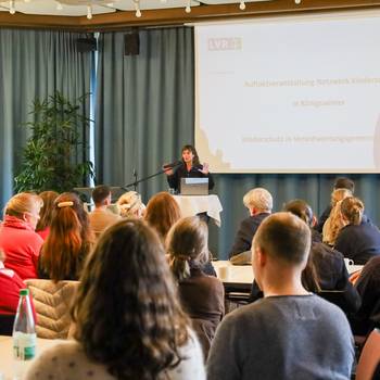 In einem Saal referiert eine Frau, vor ihr eine Gruppe von Menschen