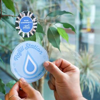 Die Refill-Aufkleber machen teilnehmende Betriebe sichtbar © Stadt Königswinter Aufkleber wird an Fenster geklebt