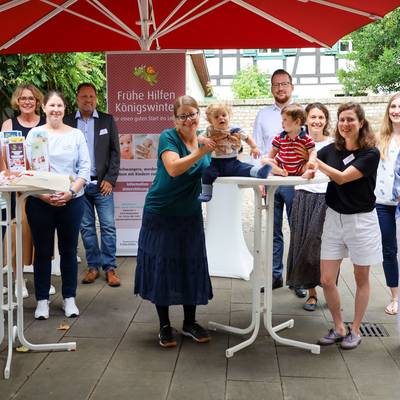 Gruppenbild aller Beteiligten. Die beiden Babies sitzen fröhlich auf dem Tisch