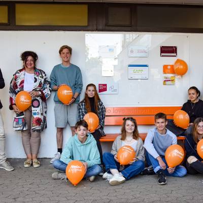„No love without respect“ – Schulleitung und Pressesprecherin sowie Schülerinnen und Schüler des CJD an der orangenen Wanderbank gegen Gewalt