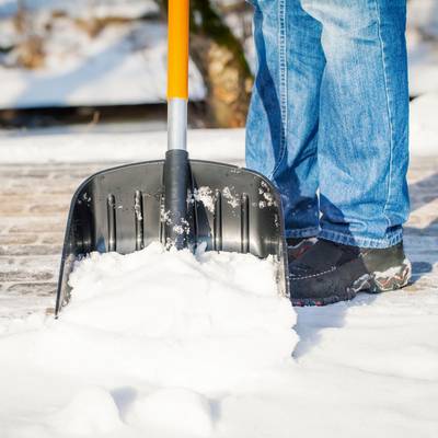 Ein Ausschnitt einer Schneeschaufel, mit der Schnee auf einem Gehweg geräumt wird