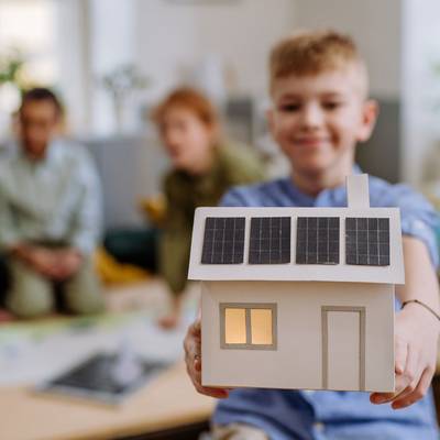 Ein Kind hält ein Model eines Hauses mit PV-Anlage in den Händen