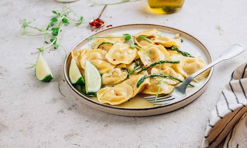 Ein Teller mit Ravioli, grünem Spargel auf einem Tisch mit Zitrone und Geschirrtuch