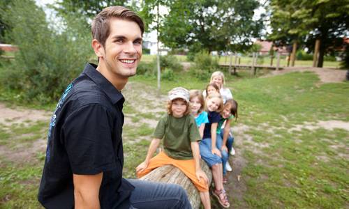Junger Mann sitzt lachend vor einer Gruppe von Kindern