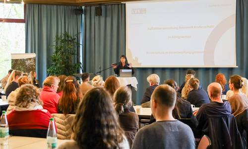 In einem Saal referiert eine Frau, vor ihr eine Gruppe von Menschen