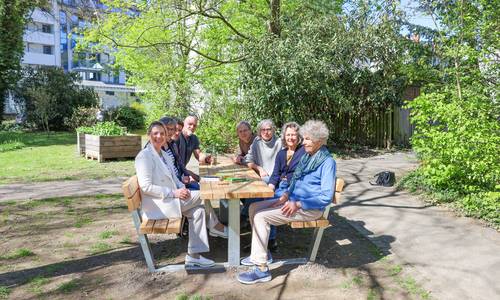 Eine Gruppe sitzt auf einer Holz-Sitzgruppe in einem Park