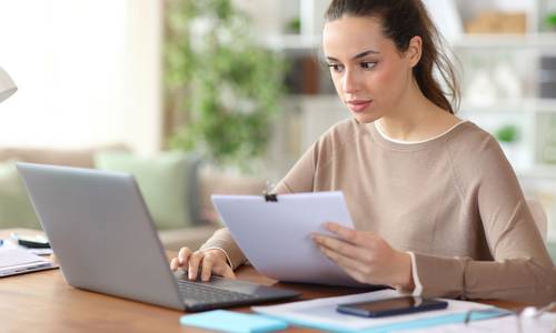 Junge Frau sitzt vor dem Laptop mit einem Formular in der Hand