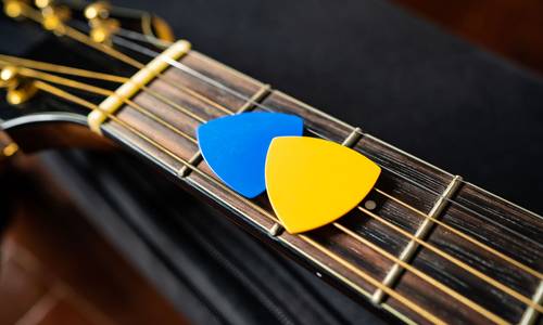 Plektrons in Gelb und Blau liegen auf einer Gitarre