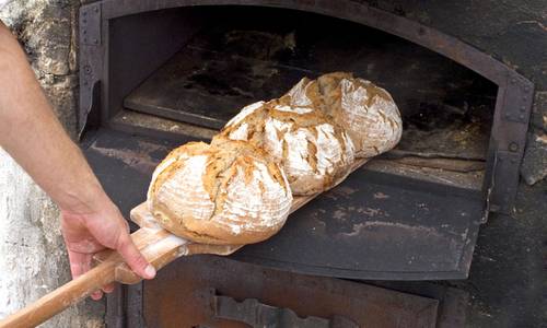 Drei gebackene Brote werden aus dem Steinofen geholt, Symboldbild