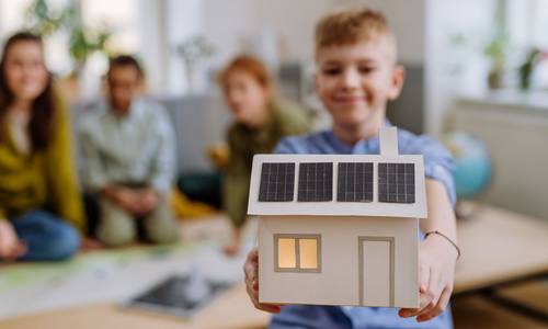 Ein Kind hält ein Model eines Hauses mit PV-Anlage in den Händen
