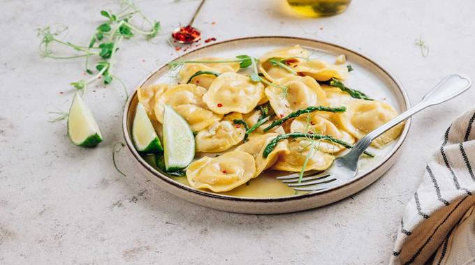 Ein Teller mit Ravioli, grünem Spargel auf einem Tisch mit Zitrone und Geschirrtuch