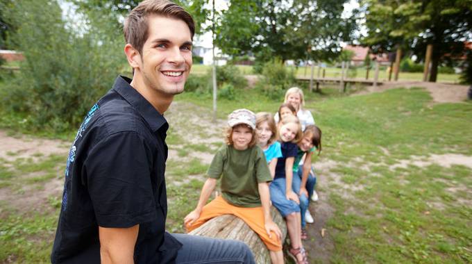 Junger Mann sitzt lachend vor einer Gruppe von Kindern
