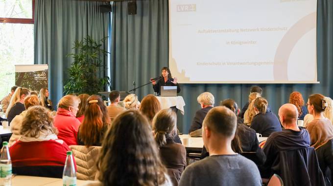 In einem Saal referiert eine Frau, vor ihr eine Gruppe von Menschen