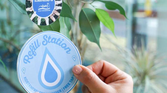 Die Refill-Aufkleber machen teilnehmende Betriebe sichtbar © Stadt Königswinter Aufkleber wird an Fenster geklebt