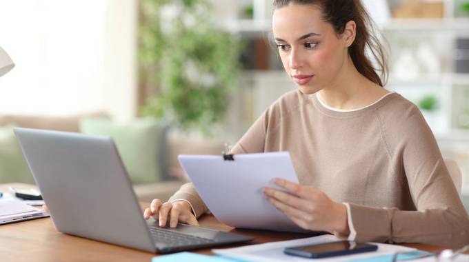 Symbolbild © Antonioguillem – stock.adobe.com Junge Frau sitzt vor dem Laptop mit einem Formular in der Hand