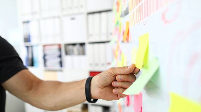 Mitmachen bei der Bürgerbeteiligung in Königswinter © H KO – stock.adobe.com Eine männliche Hand klebt ein gelbes Post-It auf eine Präsentationswand