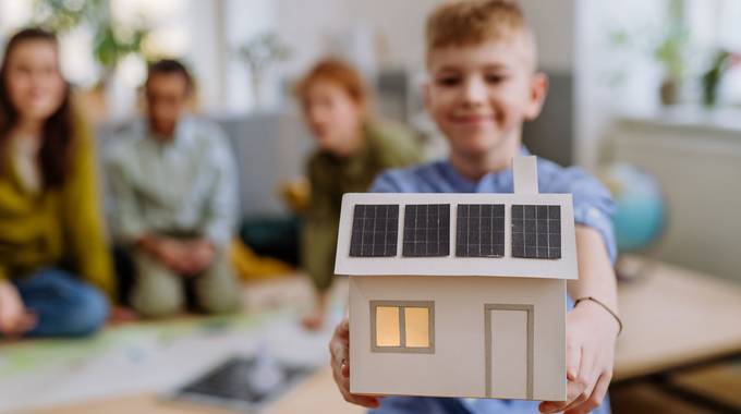 Ein Junge zeigt ein gebasteltes Papierhaus mit PV-Anlage in die Kamera