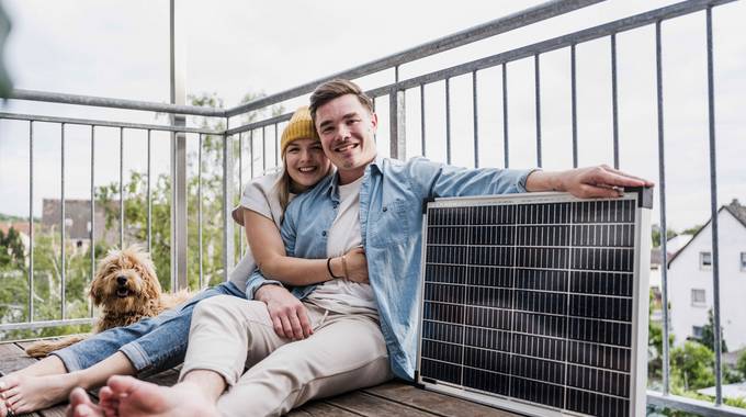 Ein lächelndes junges Paar sitzt auf dem Boden eines Balkons neben einem Solarpanel